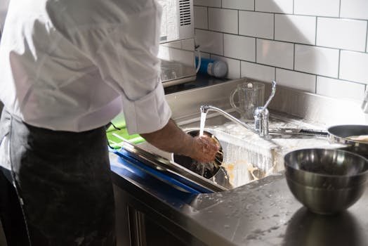 A chef washing dishes at a sink in a bright, modern kitchen setting.